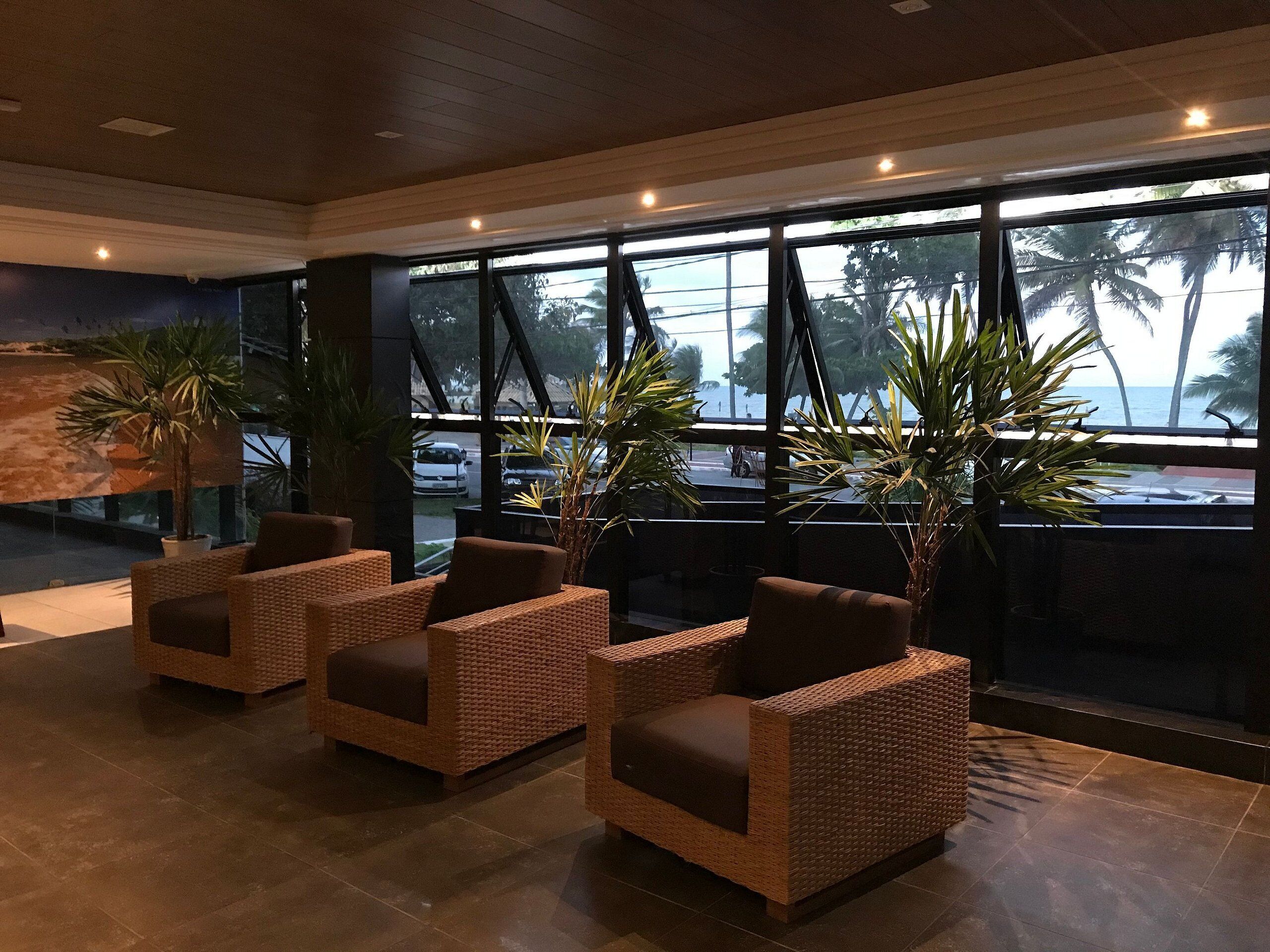 Un hall con sillas de mimbre, ventanas amplias y plantas en macetas.