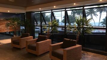 Un hall con sillas de mimbre, ventanas amplias y plantas en macetas.