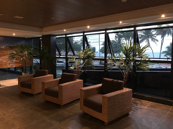 A lobby with wicker chairs, large windows, and potted plants.