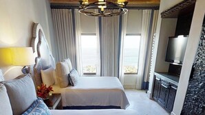A hotel room with a large bed, a TV, a desk, and a view of the sea. - Luxury Villa in 5 Star Resort (Cabo San Lucas)