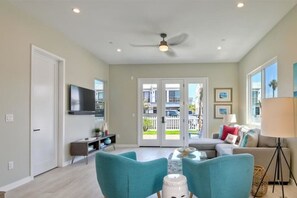 Un salon spacieux avec des fauteuils de couleur turquoise, un téléviseur à écran plat et un ventilateur de plafond.