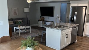 A modern kitchen with a central island, a dining area with a wooden table and chairs, a living room with a sofa and a TV, and a ceiling with recessed lighting. - Beautiful Townhouse Retreat walking distance to shakes! (Garden City)