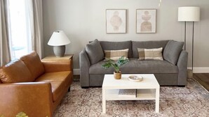 A living room with a grey sofa, a brown leather chair, a white coffee table, a ceiling fan, and two wall-mounted abstract art pieces. - Beautiful Townhouse Retreat walking distance to shakes! (Garden City)
