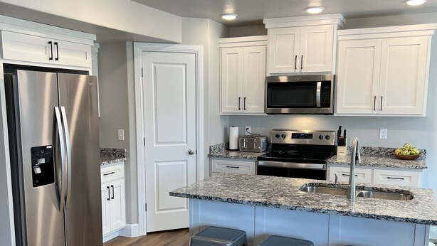 A modern kitchen with white cabinets, stainless steel appliances, and a granite countertop. - Beautiful Townhouse Retreat walking distance to shakes! (Garden City)