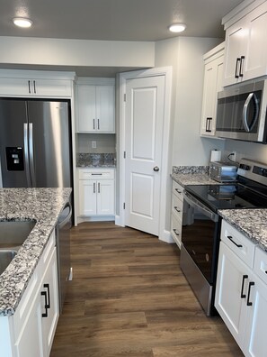 A modern kitchen with white cabinetry, granite countertops, stainless steel appliances, and a wooden floor.