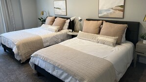 A hotel room with two beds, each with a headboard, a bedside table, and a lamp. There are two paintings on the wall above the beds. - Beautiful Townhouse Retreat walking distance to shakes! (Garden City)