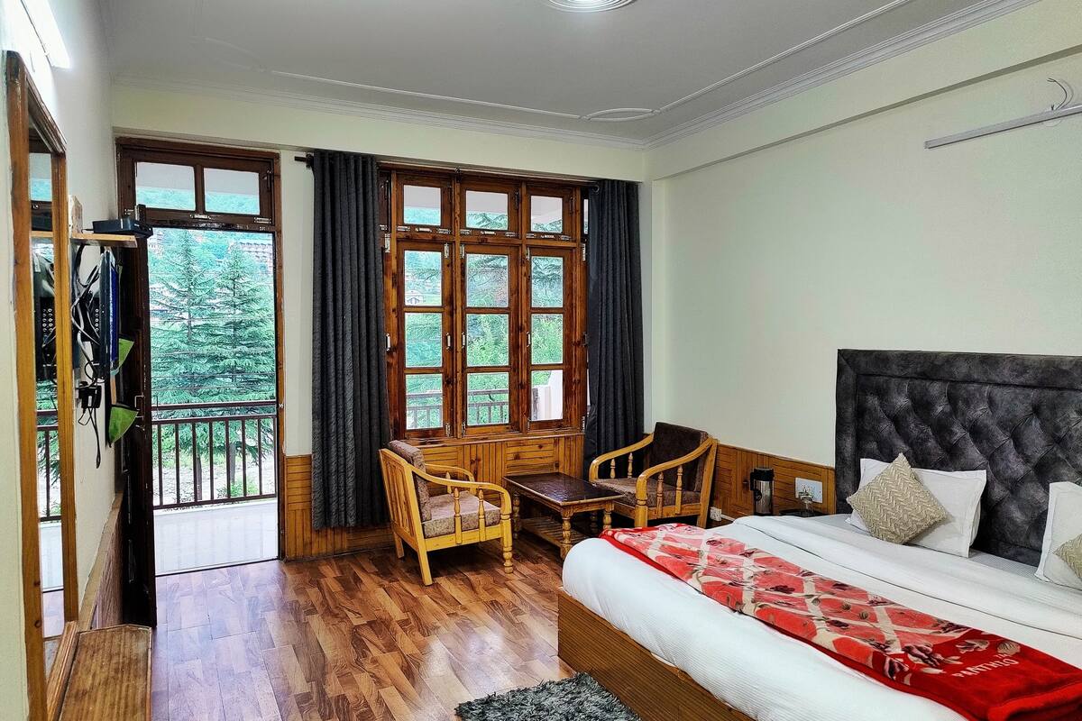 A bedroom with a bed, a wooden desk, two chairs, and a balcony with curtains.