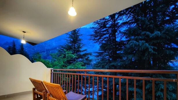 Un balcón con una silla de madera y barandilla, con vistas a una zona boscosa.