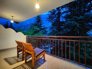 Varanda com cadeira de madeira e guarda-corpo, com vista para uma área arborizada.