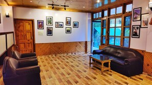 Una zona de recepción con suelo de madera en espiga, un sofá de cuero negro, una mesa de centro de madera y una pared decorada con cuadros enmarcados.
