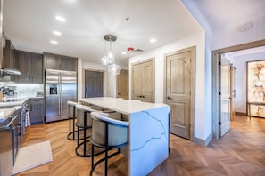 Una cocina moderna con una isla central, taburetes de bar, electrodomésticos de acero inoxidable y puertas de madera.