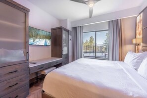 A hotel room with a bed, a desk, a wardrobe, a ceiling fan, a TV, and a balcony with a view.