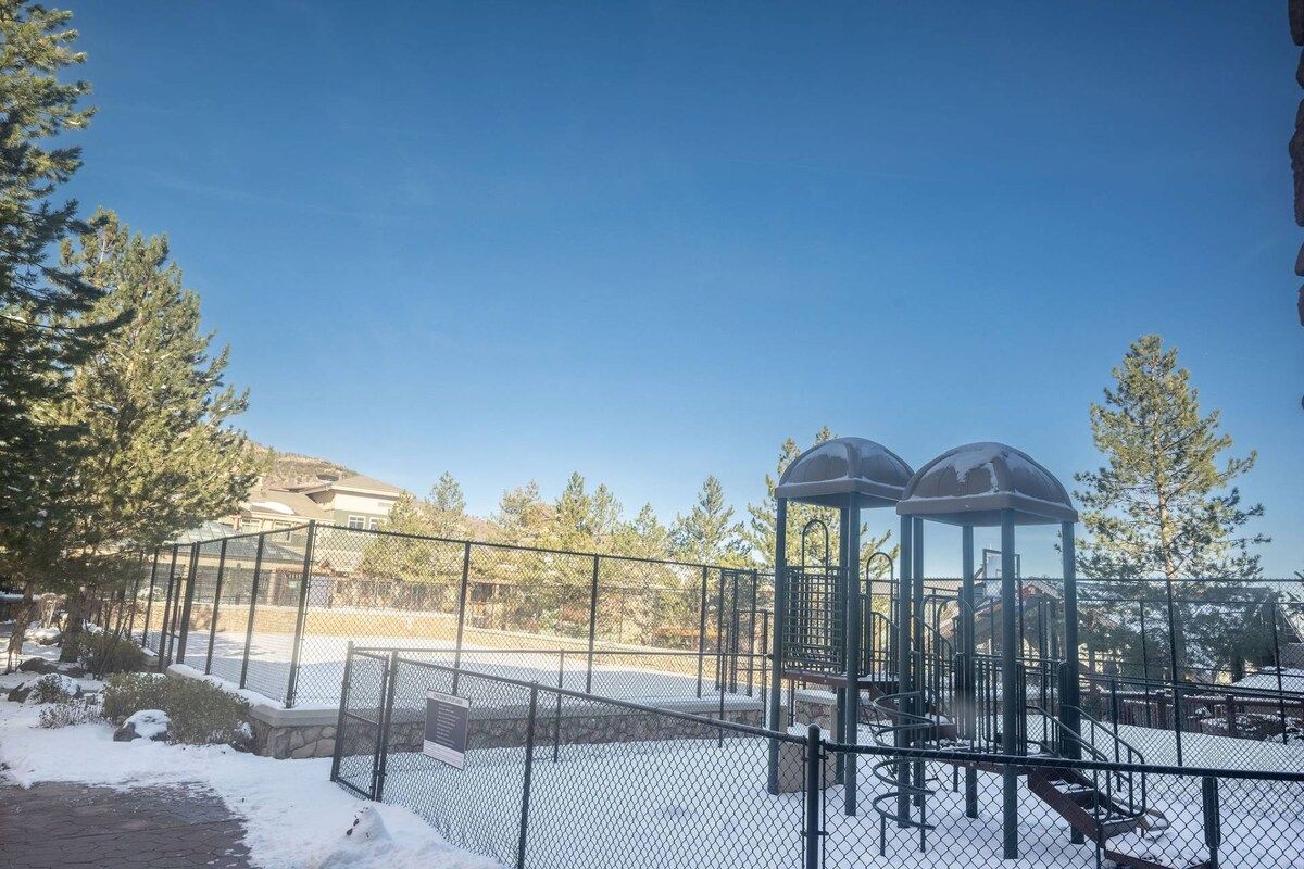 A fenced outdoor area with a playground structure, a bench, and snow on the ground.