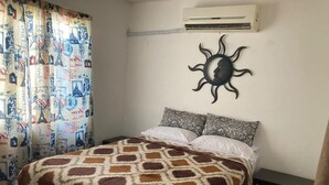 Une chambre à coucher avec une couvre-lit à motifs, une décoration murale et un rideau orné d’imprimés sur le thème du voyage.