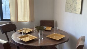 Une table de salle à manger ronde en bois, avec des assiettes carrées et des verres transparents, entourée de chaises en bois.