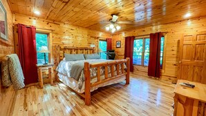 Une chambre dans une cabane en bois, avec un lit, un ventilateur de plafond et une fenêtre avec des rideaux.