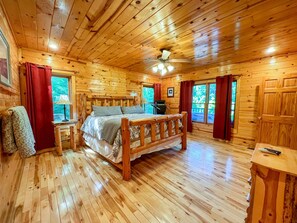 A wooden cabin bedroom with a bed, a ceiling fan, and a window with curtains.
