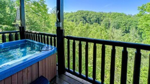 Un bain à remous sur une terrasse en bois, avec vue sur une colline boisée.