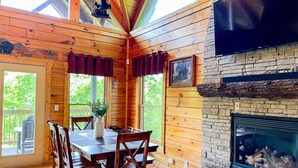 L’intérieur d’un chalet en bois comprend une table à manger, des chaises, une cheminée et une grande fenêtre.