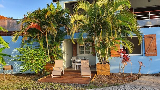 A house with a wooden deck, outdoor seating, and lush tropical plants.