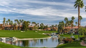 A golf course with a pond, palm trees, and buildings in the background. - Marriott Desert Springs I Studio (Palm Desert)