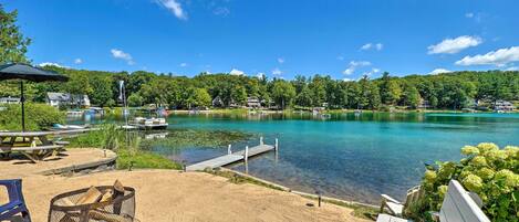 A lakeside view with a dock, picnic tables, and a fire pit.