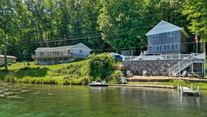 A lakeside property with a dock, a stone wall, and a house with a balcony. - Lakefront Newaygo Home - Private Dock, Kayaks (Newaygo)
