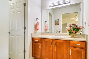 A bathroom with a white door, wooden cabinets, a sink, and a mirror with lights above it. - Foley Getaway w/ Fenced Yard - 13 Mi to Beaches! (Foley)