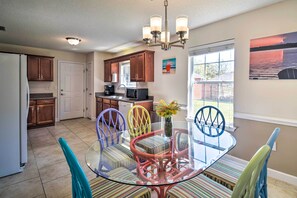 A modern kitchen with wooden cabinets, a glass dining table, colorful chairs, and a chandelier. - Foley Getaway w/ Fenced Yard - 13 Mi to Beaches! (Foley)