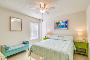 A bedroom with a bed, a green nightstand, a green bench, a ceiling fan, a window with blinds, and a painting of a beach scene. - Foley Getaway w/ Fenced Yard - 13 Mi to Beaches! (Foley)