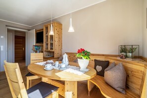 Un coin repas chaleureux avec une table en bois, des chaises, un banc et des lampes suspendues.