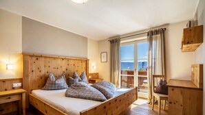 Un lit en bois avec une tête de lit, des tables de chevet, une chaise et une armoire en bois, dans une pièce dotée d’une grande fenêtre offrant une vue dégagée.