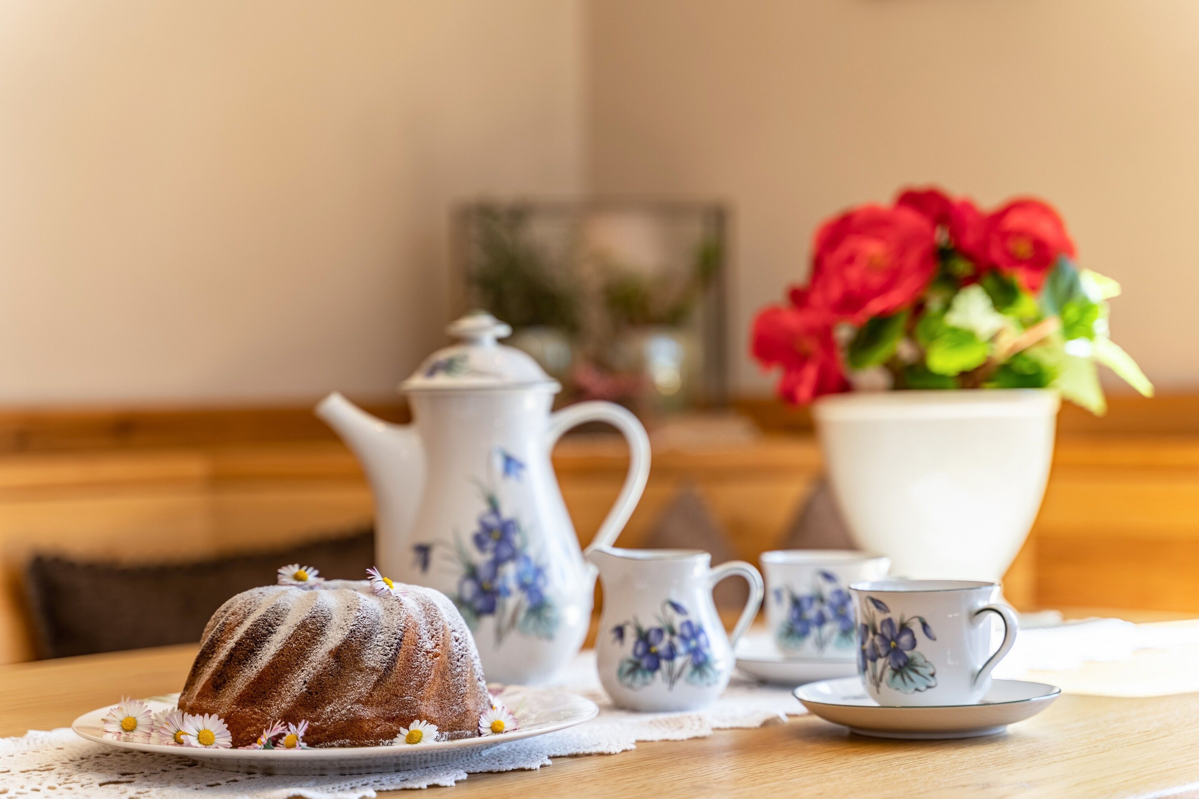 A table with a bundt cake, teapot, cups, and a vase of flowers.