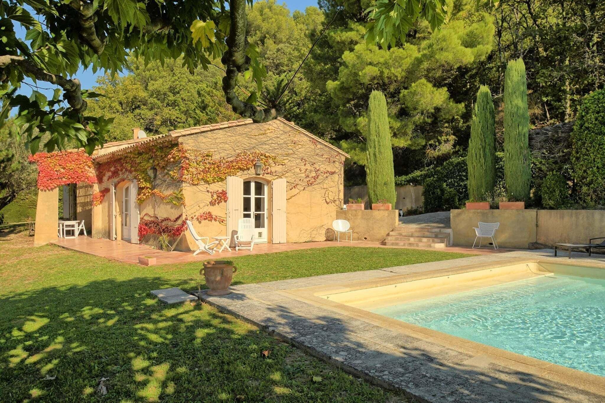 Una casa con piscina, un patio con sillas y un jardín con árboles.