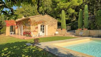 Una casa con piscina, un patio con sillas y un jardín con árboles.