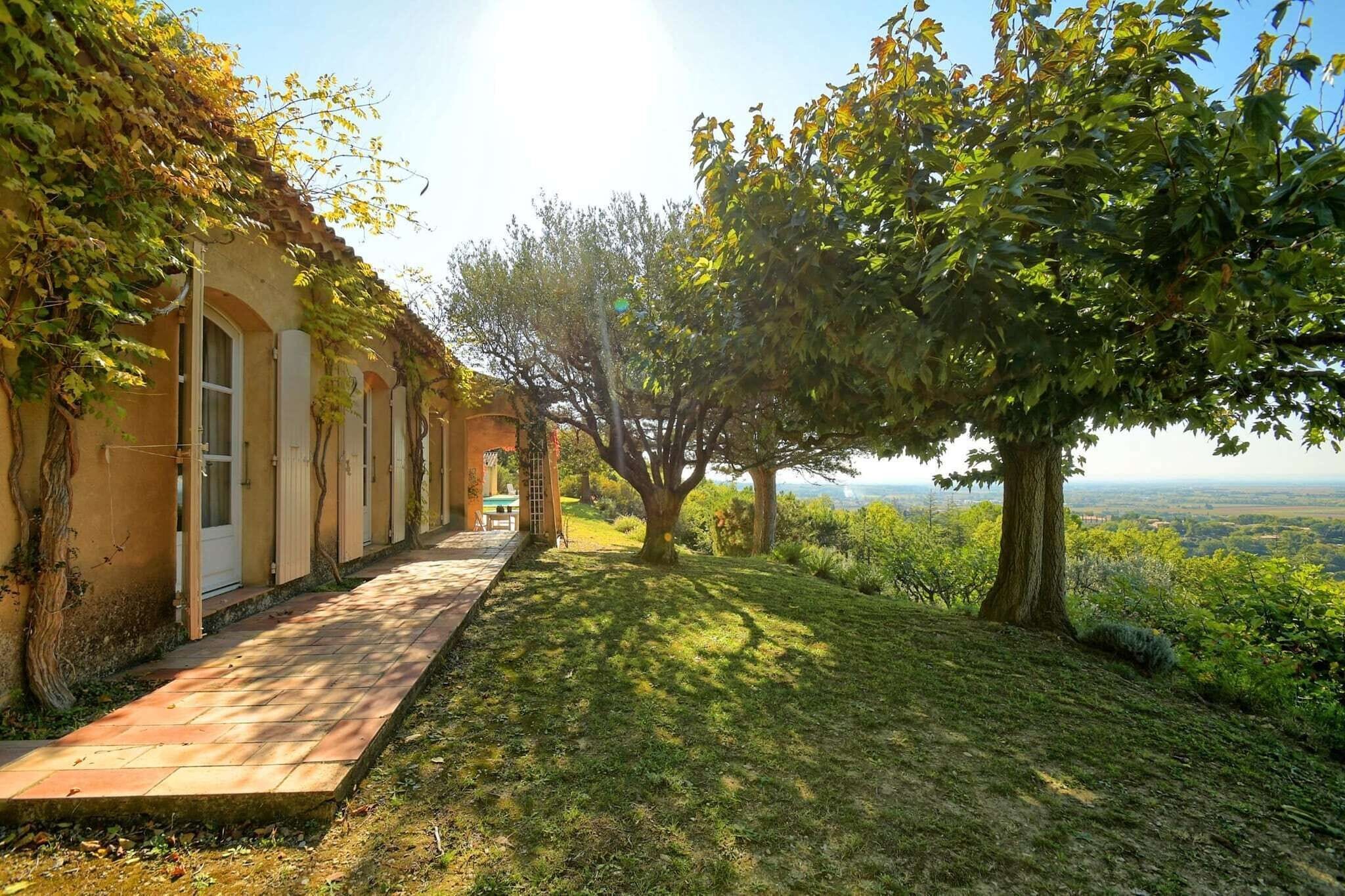 Un sendero conduce a un edificio con ventanas arqueadas y un porche cubierto, rodeado de árboles y vistas del paisaje.