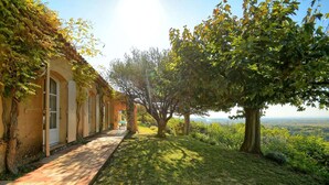 A pathway leading to a building with arched windows and a covered porch, surrounded by trees and a view of the landscape. - Sunny holiday home in Provence with pool (Séguret)