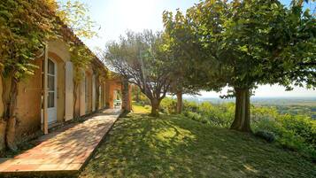 Un sendero conduce a un edificio con ventanas arqueadas y un porche cubierto, rodeado de árboles y vistas del paisaje.