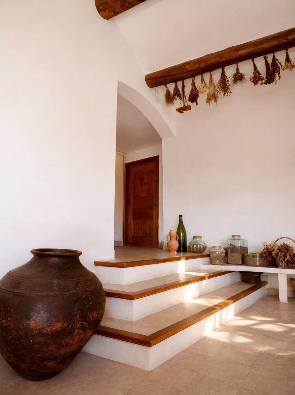 Una escalera que lleva a una puerta, un jarrón grande y varios recipientes en una estantería.