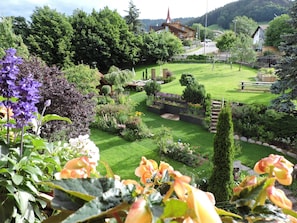 Un jardin bien entretenu, avec différentes plantes et une pelouse, une clôture en bois et, au fond, un bâtiment doté d’un toit en pente.