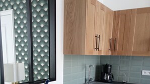 A modern kitchen with wooden cabinets, a black countertop, and a dining table set for two. - In the heart of the city Gîte "La cour des trois rois" (The court of the three kings) (Villedieu-les-Poêles-Rouffigny)