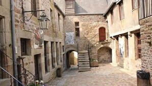 A narrow stone alleyway with a staircase leading to an upper level, flanked by buildings with arched doorways and windows. - In the heart of the city Gîte "La cour des trois rois" (The court of the three kings) (Villedieu-les-Poêles-Rouffigny)