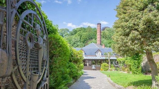 A pathway leading to a building with a chimney, surrounded by greenery and a metal gate. - In the heart of the city Gîte "La cour des trois rois" (The court of the three kings) (Villedieu-les-Poêles-Rouffigny)