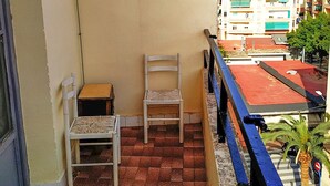 Un balcón con una silla, una mesa pequeña, piso de baldosas y vistas a edificios en la distancia.