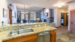 A kitchen with granite countertops, stainless steel appliances, wooden cabinets, and a stone fireplace. - Big Horn Lodge 501 - Luxury Two Bedroom (Truckee)