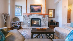A cozy living room with a stone fireplace, a television mounted above it, and comfortable seating. - Big Horn Lodge 501 - Luxury Two Bedroom (Truckee)