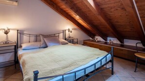 Une chambre à coucher avec un plafond en pente, un lit recouvert d’une courtepointe, des tables de chevet et des lampes fixées au mur.