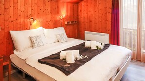 A wooden-paneled bedroom with a bed, white linens, a dark throw blanket, and towels. - Vacation home Dorine by Interhome (Nendaz)
