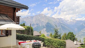 A patio with a barbecue grill, outdoor table, and umbrella, overlooking a mountainous landscape. - Vacation home Dorine by Interhome (Nendaz)
