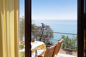 Un balcone con tavolo e sedie, affacciato su un corpo d'acqua e alberi.